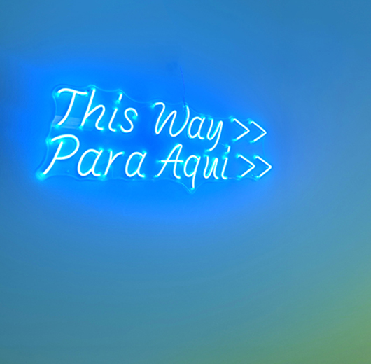 "This way / Para aqui" neon sign at The Outreach House
